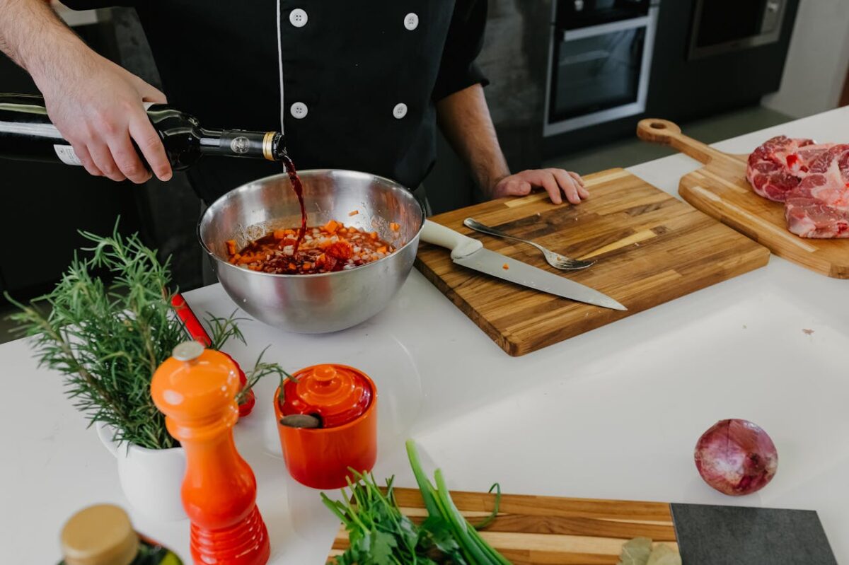 Chef pouring red wine into bowl with herbs and spices for marinade preparation.