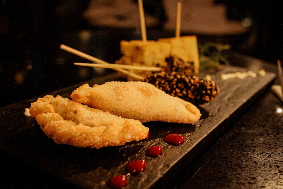 Delicious gourmet dish featuring fried empanadas and skewers on a dark serving platter.